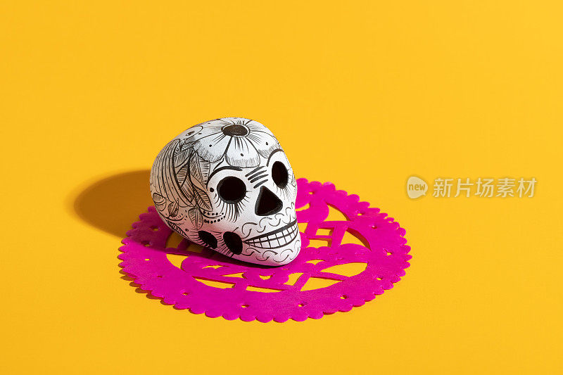 死亡的一天的陶器头骨(calavera)在粉红色的皮卡多在黄色的背景，Dia de Muertos的背景